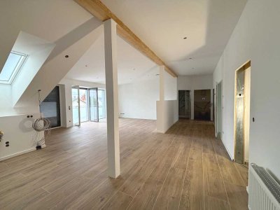 Moderne DG-Wohnung, Wohnzimmer mit offener Küche und großem Balkon.